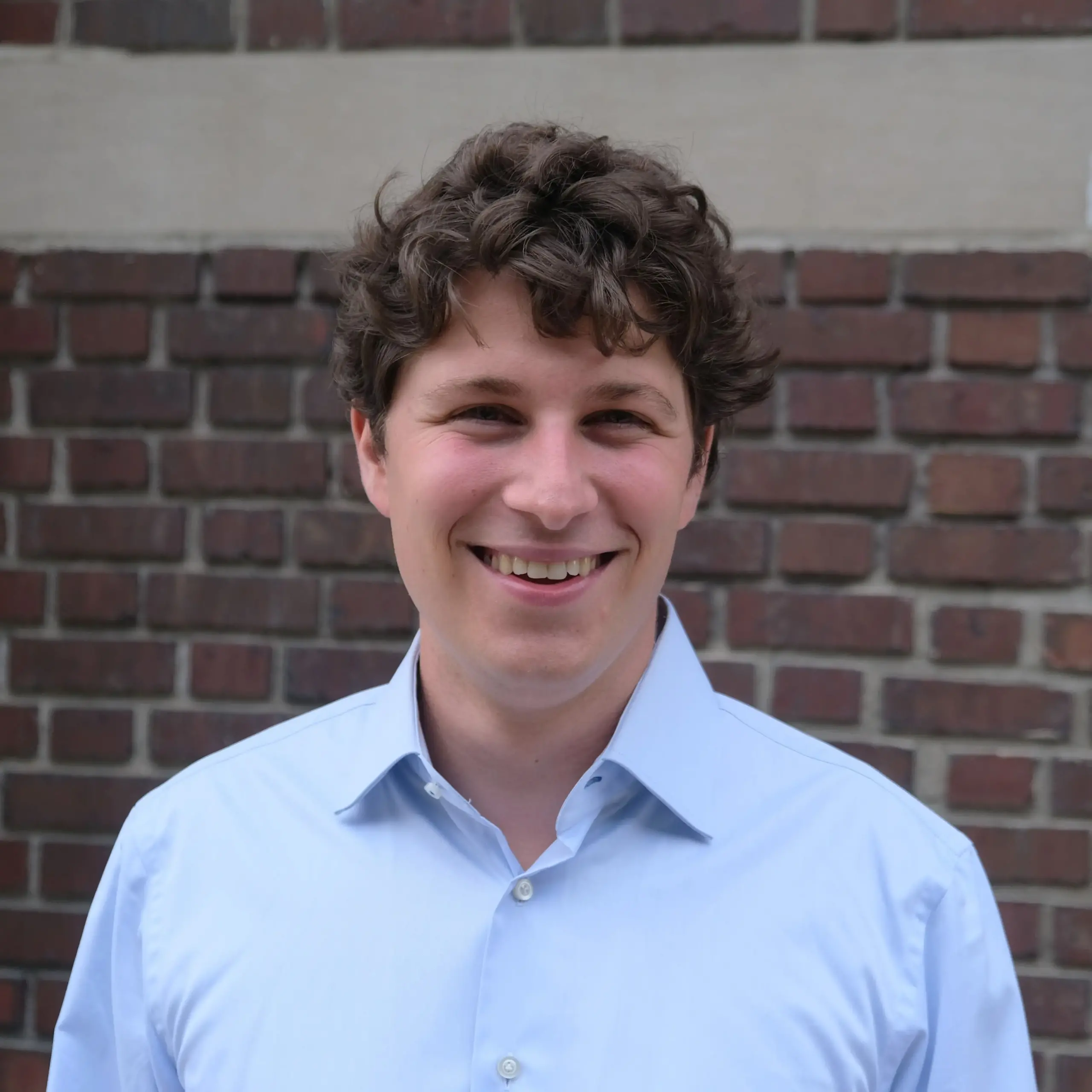 headshot of joe in collared blue shirt with a brick background