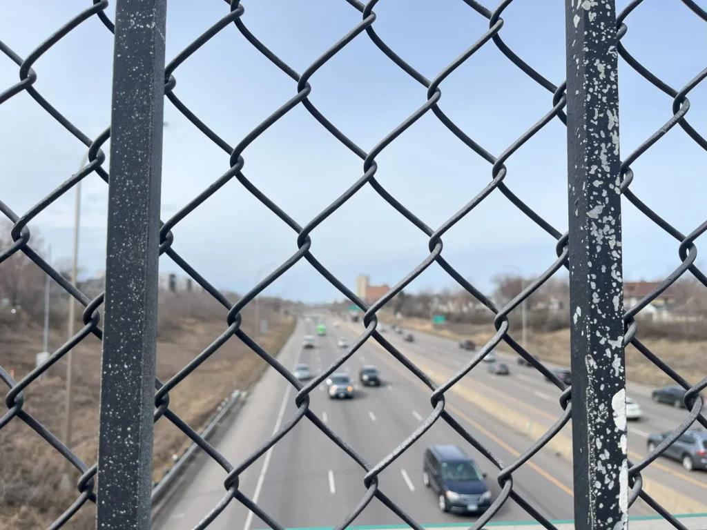 view of I-94 from a pedestrian bridge in rondo through a chain link fence